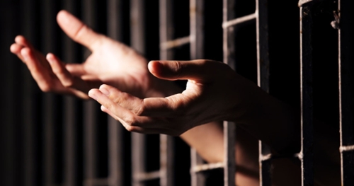 Picture of two hands reaching out through prison bars.